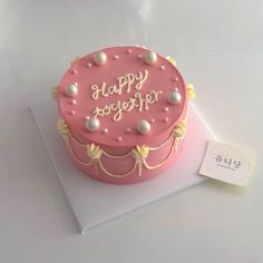 a pink birthday cake sitting on top of a white tablecloth next to a tag