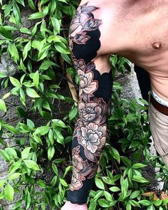 a man with tattoos on his arm and leg is standing in front of some bushes