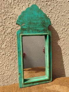 a green mirror sitting on top of a wooden table next to a white stucco wall