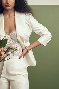 a woman in a white suit holding a bouquet of flowers with her hands on her hips