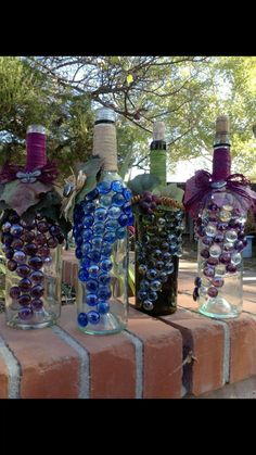 three wine bottles are sitting on top of a brick wall and decorated with glass beads