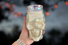 a hand holding a glass jar with a skull on it's side and lights in the background