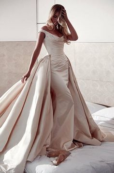 a woman in a white dress standing on a bed with her hands behind her head