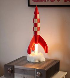 a red and white rocket ship sitting on top of a stereo box next to a wall