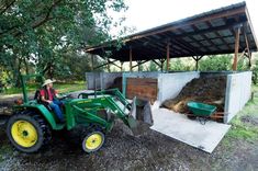 a man riding on the back of a green tractor next to a pile of hay