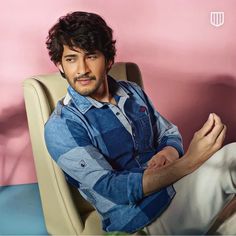 a man sitting in a chair with his legs crossed and looking at the camera while wearing a blue shirt