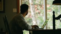 a man sitting in front of a laptop computer on top of a desk next to a lamp