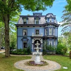 a large blue house with a fountain in front of it and trees around the yard