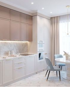 a kitchen with marble counter tops and white cabinets, along with a dining room table surrounded by blue chairs