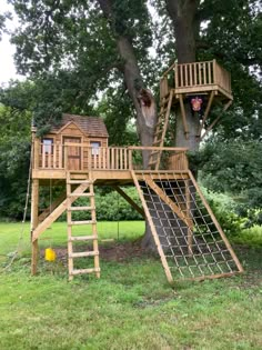 a tree house with a slide and climbing net on the bottom level is shown in front of a large tree