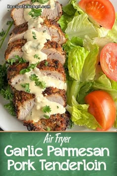 a white plate topped with meat covered in sauce and lettuce next to a salad