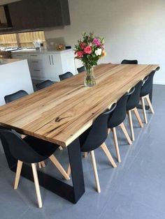 a wooden table surrounded by black chairs and a vase with flowers in it on the floor