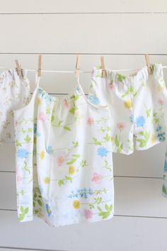 three baby clothes hanging on the clothesline with flowers all over them and one is white