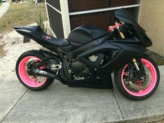 a black motorcycle with pink wheels parked in front of a garage door on the sidewalk