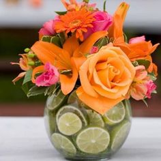 an arrangement of flowers and limes in a glass vase on a white tablecloth