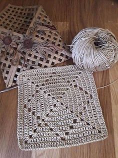 two crocheted squares are sitting on the floor next to yarn