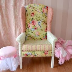 a chair and ottoman in a room with pink flowers on the wall, two white pom poms are next to it