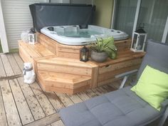 a hot tub sitting on top of a wooden deck next to a chair and potted plant