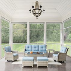 an outdoor living room with blue cushions and wicker furniture on the porch, surrounded by large windows