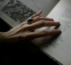 a woman's hand is holding an open book with a ring on it,