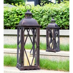 two metal lanterns sitting on the side of a road next to some grass and bushes