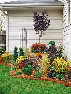 a garden with lots of different types of flowers and plants in the grass next to a house