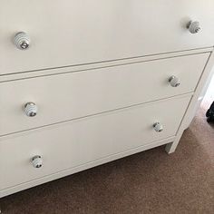 a white dresser with drawers and knobs in a living room or bedroom area next to a carpeted floor