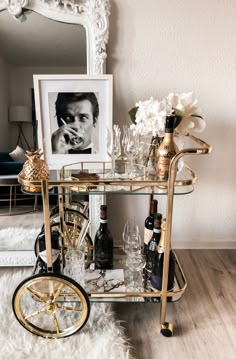 a gold bar cart with wine glasses and bottles on it in front of a mirror