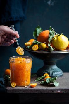 a person is spooning orange marmalade into a jar filled with tangerines