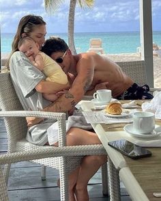 a man and woman hugging each other while sitting at a table in front of the ocean