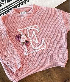 a pink sweater with a flower on the front and an embroidered t - shirt on the back