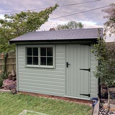 a small shed with the door open and windows on it's side, next to a garden