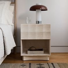 a nightstand with a lamp on top of it next to a bed