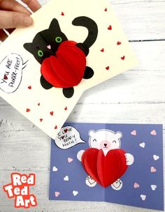 someone is holding up a red heart shaped card with a black cat and bear on it