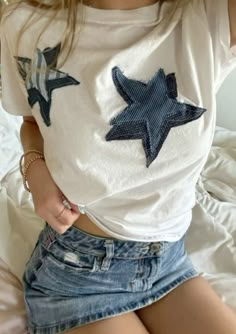 a woman wearing a white shirt with blue stars on the front and back, sitting on a bed