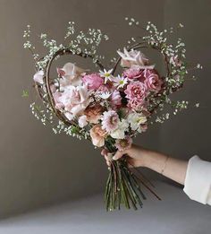 a person holding a bouquet of flowers in front of a heart shaped arrangement with baby's breath