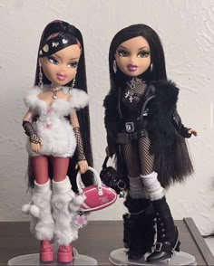 two dolls are standing next to each other on a table with one holding a purse