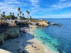 people are walking on the beach next to the water and palm trees in the background