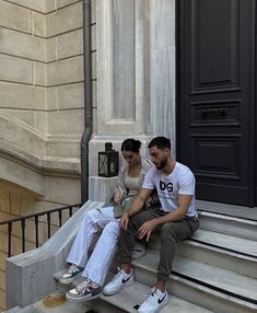 a man and woman sitting on steps next to each other in front of a building