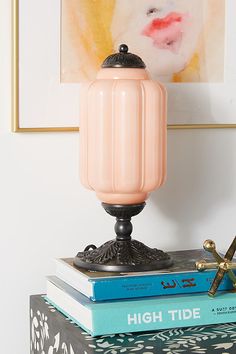 a pink lamp sitting on top of a stack of books in front of a painting