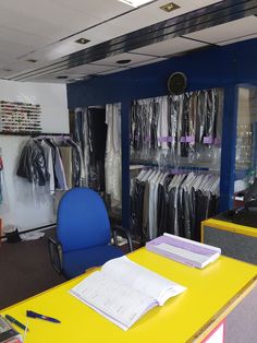 a room filled with lots of clothes next to a yellow desk and blue office chair