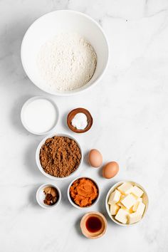 ingredients to make chocolate cake laid out in bowls on a marble countertop, including eggs, butter, flour, and sugar