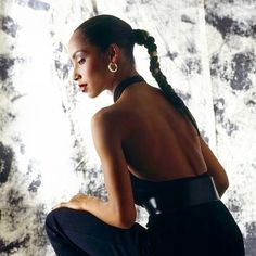 a woman sitting on the ground with her hair in a pony tail style ponytail, wearing black pants and a halter top