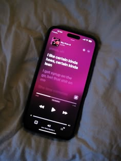 a cell phone sitting on top of a bed covered in white sheets and pink lighting