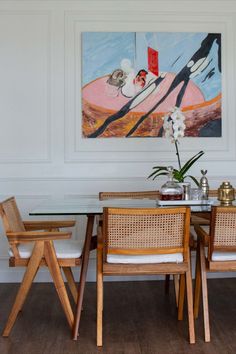 a dining room table and chairs in front of a painting on the wall above it