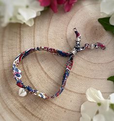 a cross bracelet with red, white and blue beads is sitting on a piece of wood