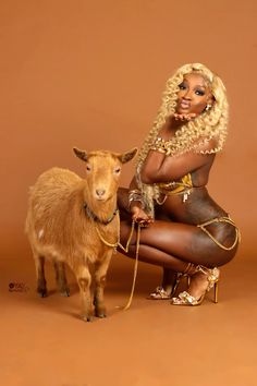 a woman kneeling down next to a goat on a brown background in front of a tan backdrop