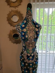 a mannequin made out of buttons and beads in front of a window with mirrors on the wall