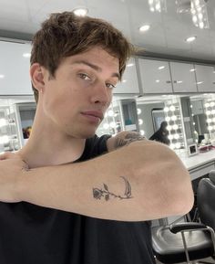 a man with a tattoo on his arm in front of a hairdresser's mirror