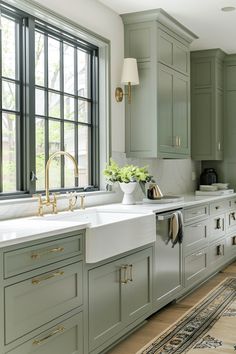 a kitchen with green cabinets and white counter tops, gold faucets and brass pulls